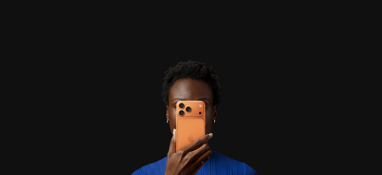 Eine Person hält ein iPhone 17 Pro vor ihr Gesicht, wobei die Rückseite nach außen zeigt; die Farbe ist Cosmic Orange.